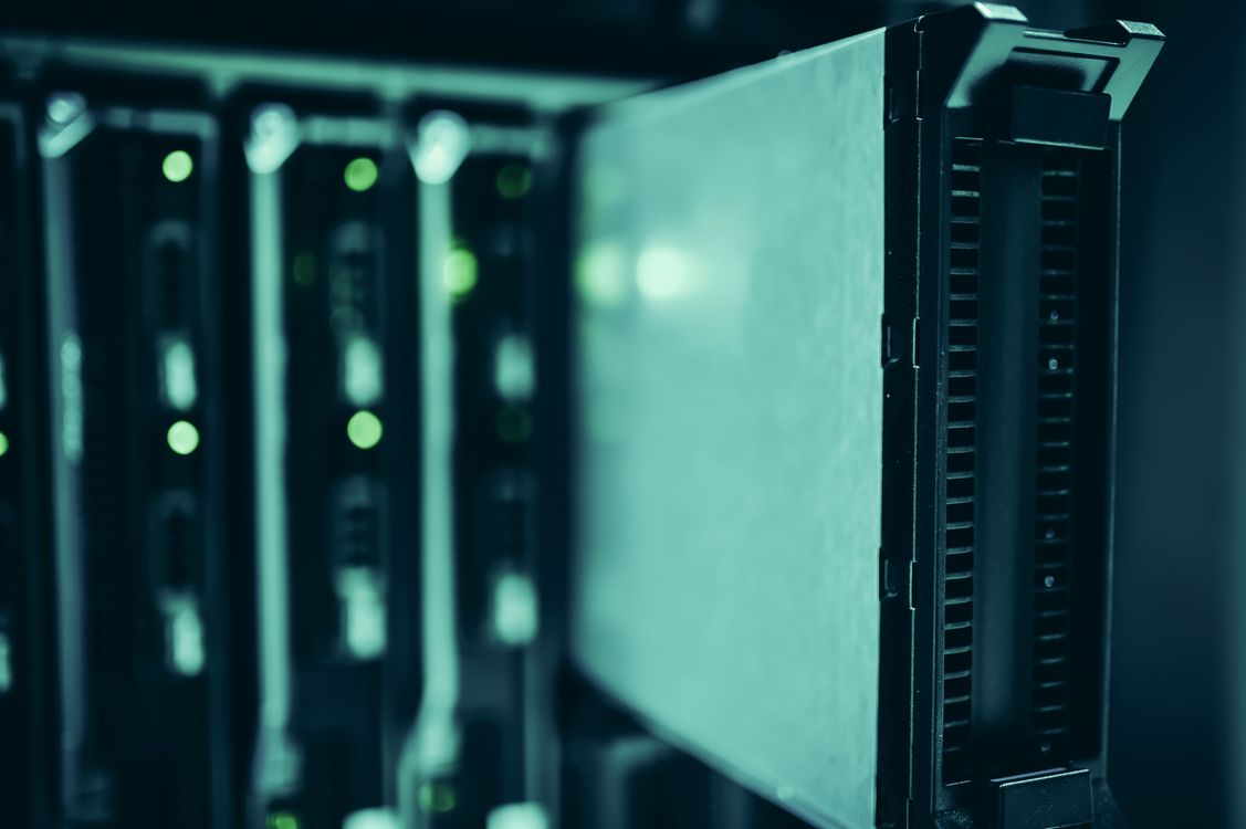 Close-up of a server blade being inserted into a data center rack, illuminated with cool blue-teal lighting.