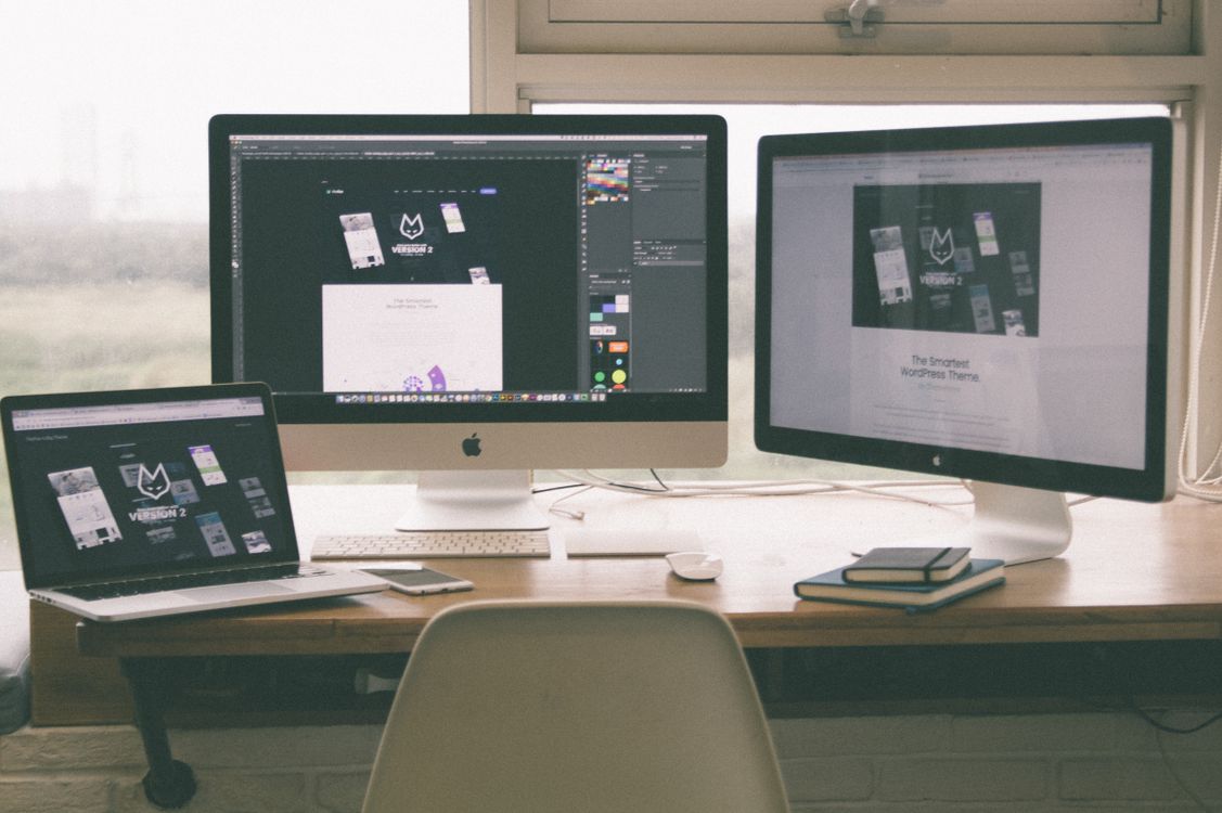 A modern desk workspace with multiple monitors and a laptop displaying a web design project.